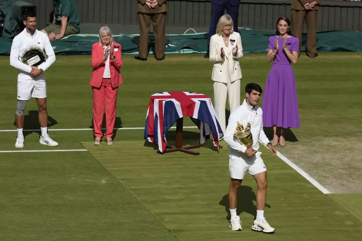 Carlos Alcaraz of Spain holds his trophy as he goes to an on court interview after defeating Novak Djokovic of Serbia, at left, in the men's singles final at the Wimbledon tennis championships in London, Sunday, July 14, 2024. At right is Kate, Princes of Wales. (AP Photo/Mosa'ab Elshamy)