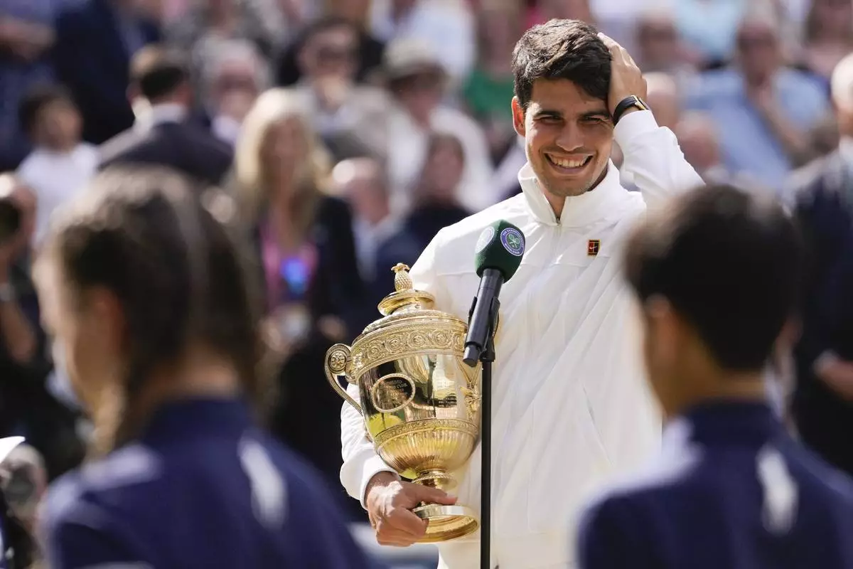 Carlos Alcaraz of Spain reacts as he is interviewed on court as he holds his trophy after defeating Novak Djokovic of Serbia in the men's singles final at the Wimbledon tennis championships in London, Sunday, July 14, 2024. (AP Photo/Alberto Pezzali)