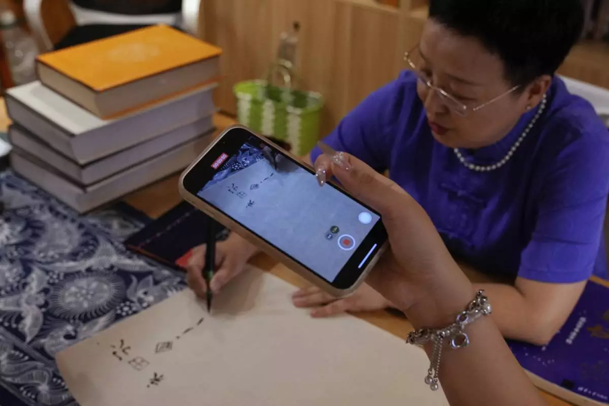A student uses a smartphone to film Xu Yan, an author of a textbook on nüshu, a centuries-old secret script, demonstrating to write nüshu calligraphy at her studio in Beijing on July 11, 2024. (AP Photo/Andy Wong)