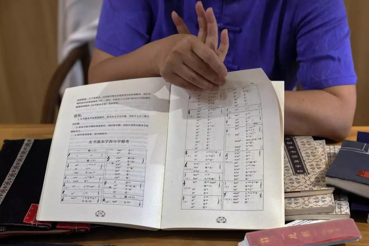 Xu Yan, an author of a textbook on nüshu, a centuries-old secret script, shows a book of nüshu calligraphy to the visiting university students at her studio in Beijing on July 11, 2024. (AP Photo/Andy Wong)