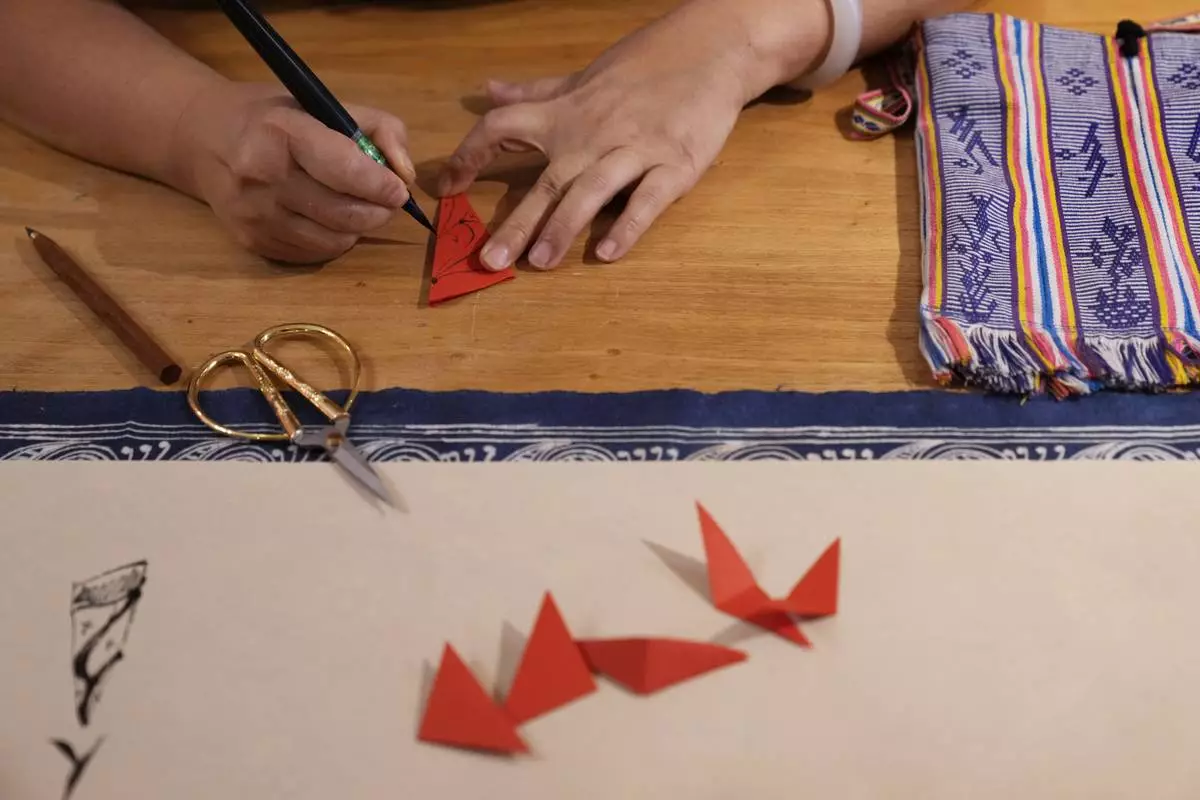 Xu Yan, an author of a textbook on nüshu, a centuries-old secret script, writes nüshu on paper cuttings at her studio in Beijing on July 11, 2024. (AP Photo/Andy Wong)