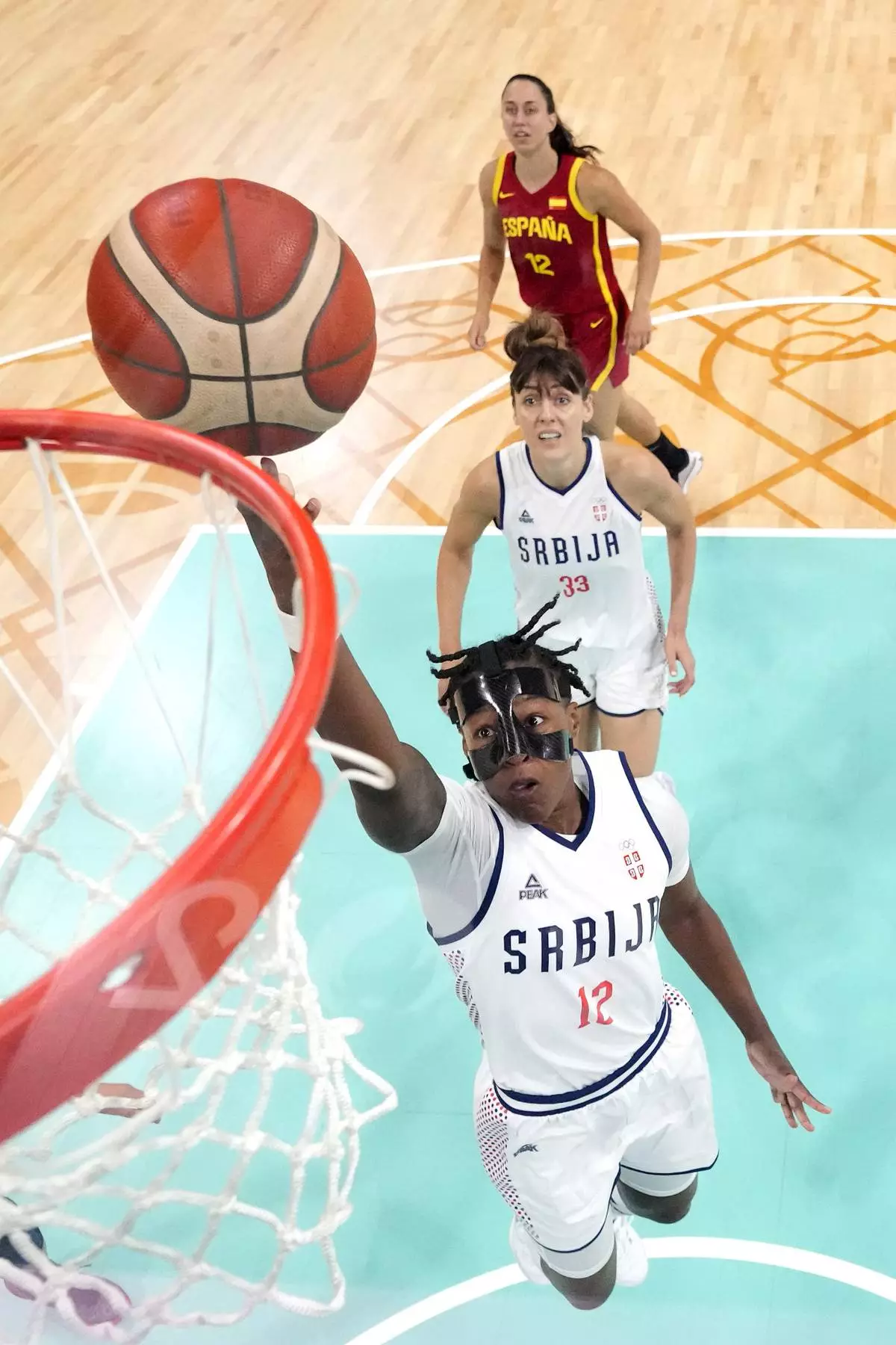 Serbia's Yvonne Anderson, below, shoots as Serbia's Tina Kajisnik, center, and Spain's Maite Cazorla watch during a women's basketball game at the 2024 Summer Olympics, Saturday, Aug. 3, 2024, in Villeneuve-d'Ascq, France. (AP Photo/Michael Conroy, Pool)