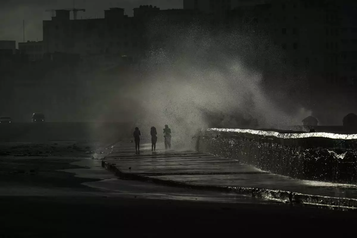 People walk along the boardwalk as waves crash during a power outage in Havana, Monday, Oct. 21, 2024. (AP Photo/Ramon Espinosa)