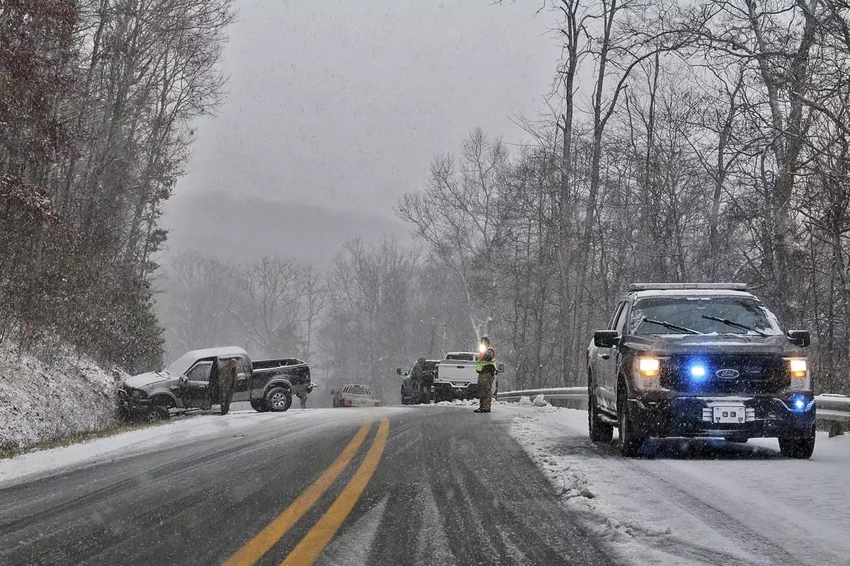 A driver, left, waits for his truck to be removed from an accident site after sliding into a hillside during snow showers, Thursday, Nov. 21, 2024, near Quinwood, W.Va. (Jenny Harnish/The Register-Herald via AP)