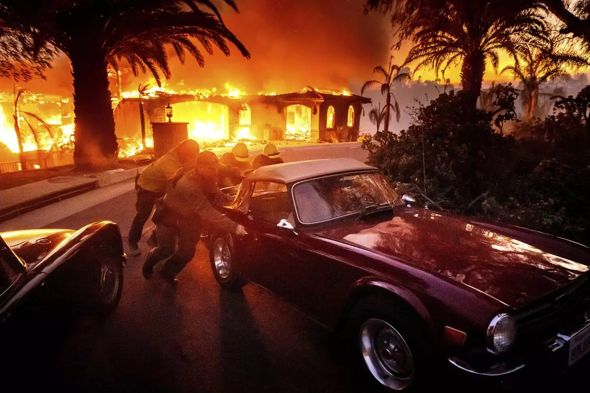 CORRECTS CAR - Firefighters and sheriff's deputies push a vintage car away from a burning home as the Mountain Fire burns in Camarillo, Calif., on Wednesday, Nov. 6, 2024. (AP Photo/Noah Berger)