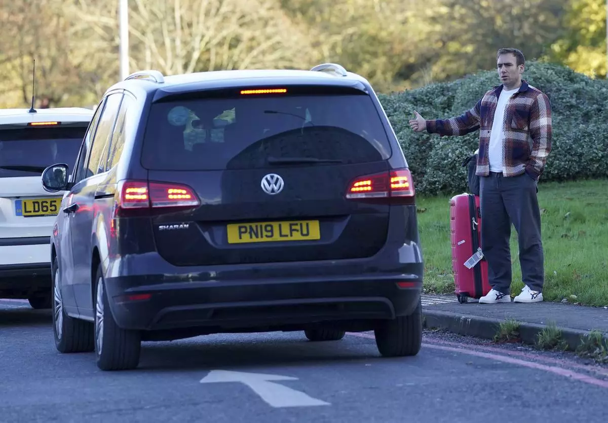 A passenger hitchhikes outside Gatwick airport, where flights have been cancelled and delayed after a "suspected prohibited item" was found in luggage, near Crawley, England, Friday Nov. 22, 2024. (Gareth Fuller/PA via AP)