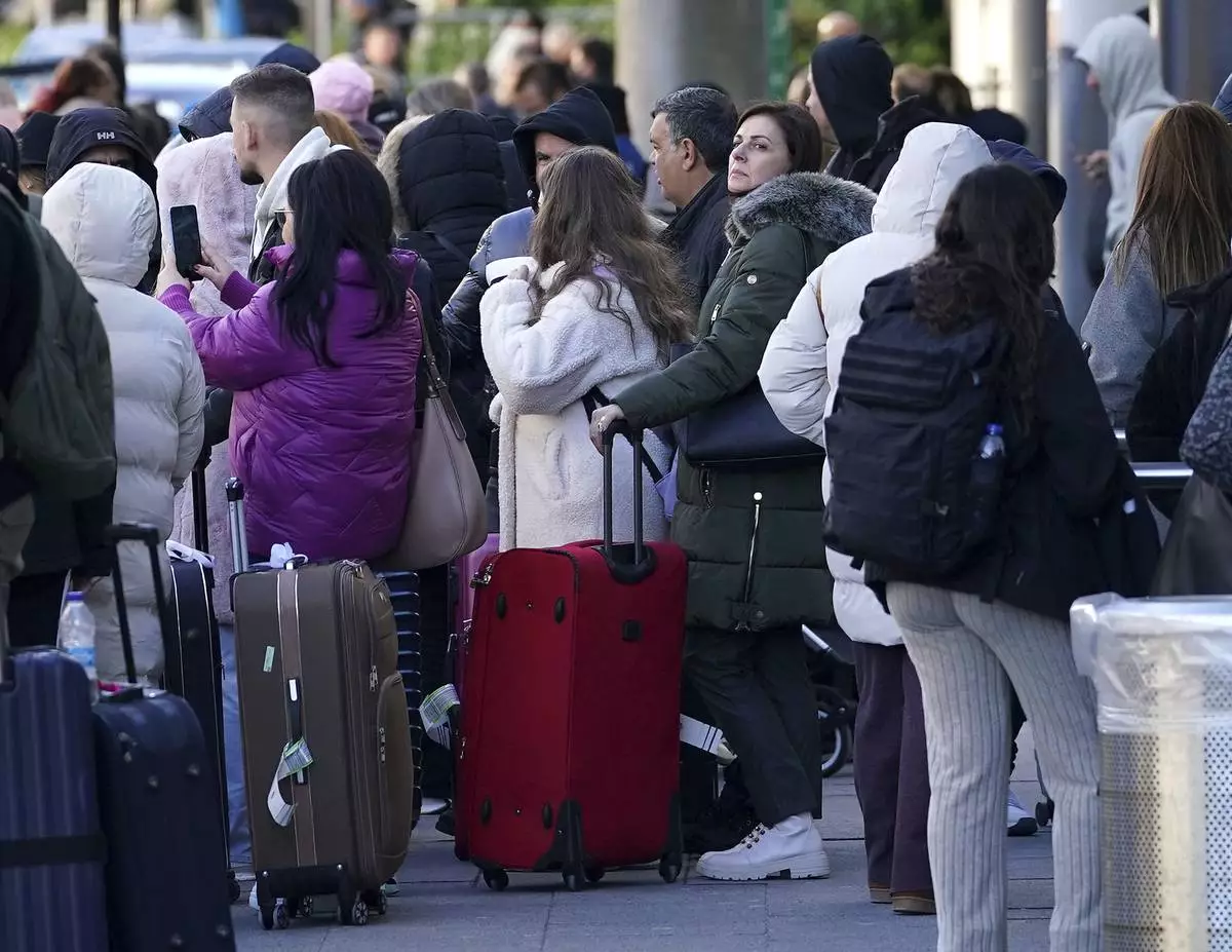 Passengers stand outside Gatwick airport, where flights have been cancelled and delayed after a "suspected prohibited item" was found in luggage, in Crawley, England, Friday Nov. 22, 2024. (Gareth Fuller/PA via AP)
