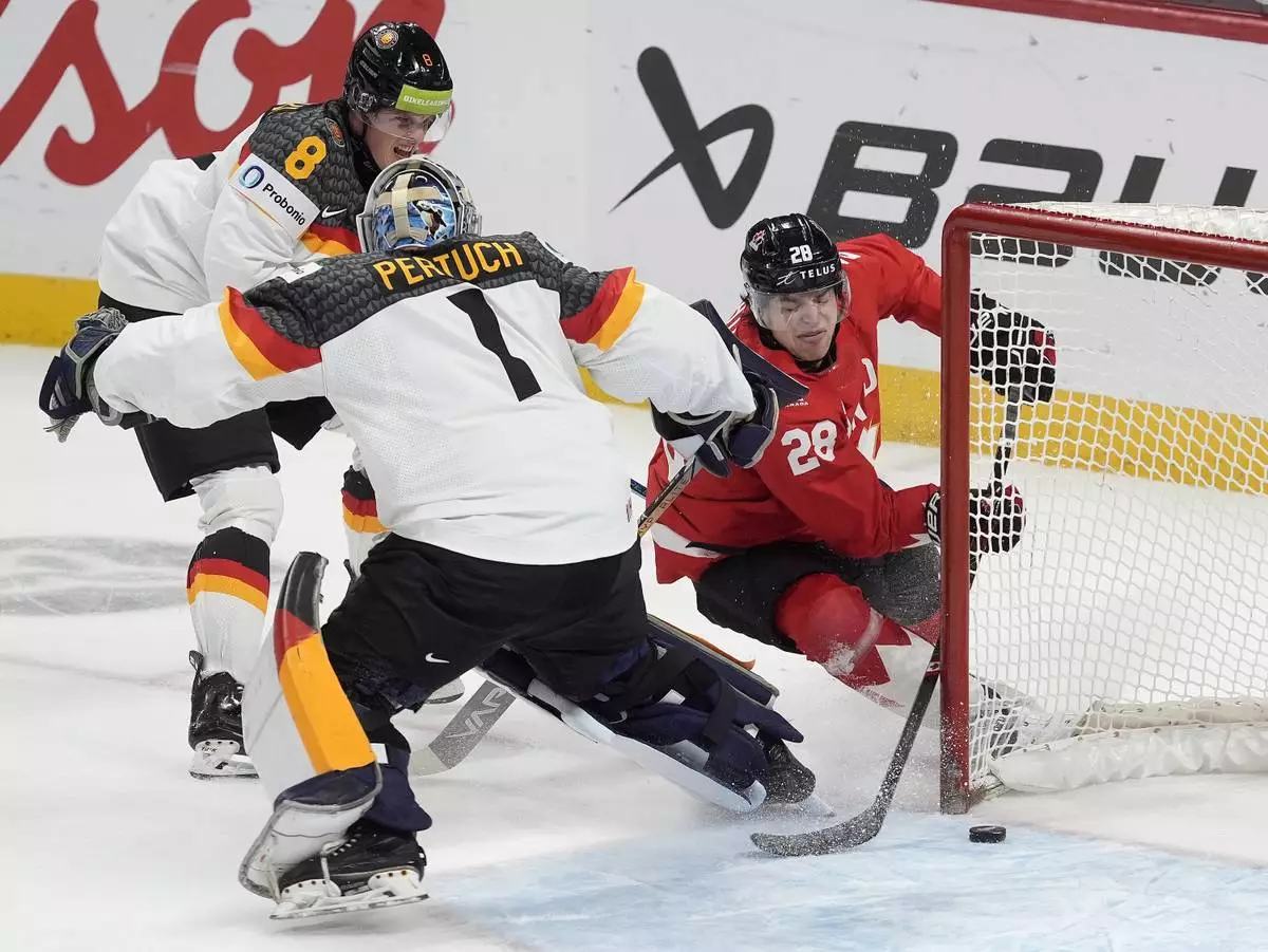 Canada forward Mathieu Cataford (28) tries to get the puck into the net behind Germany goaltender Nico Pertuch (1) as he is pressured by Germany forward Noah Samanski (8) during first-period IIHF World Junior Hockey Championship tournament game action in Ottawa, Ontario, Sunday, Dec. 29, 2024. (Adrian Wyld/The Canadian Press via AP)