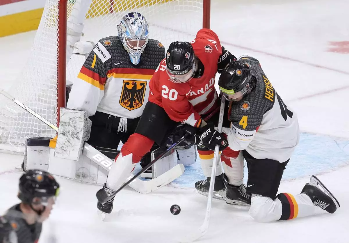 Canada forward Ethan Gauthier (20) tries to deflect the puck past Germany goaltender Nico Pertuch, left, as he is pressured by Germany defenseman Max Hense (4) during second-period IIHF World Junior Hockey Championship tournament game action in Ottawa, Ontario, Sunday, Dec. 29, 2024. (Adrian Wyld/The Canadian Press via AP)