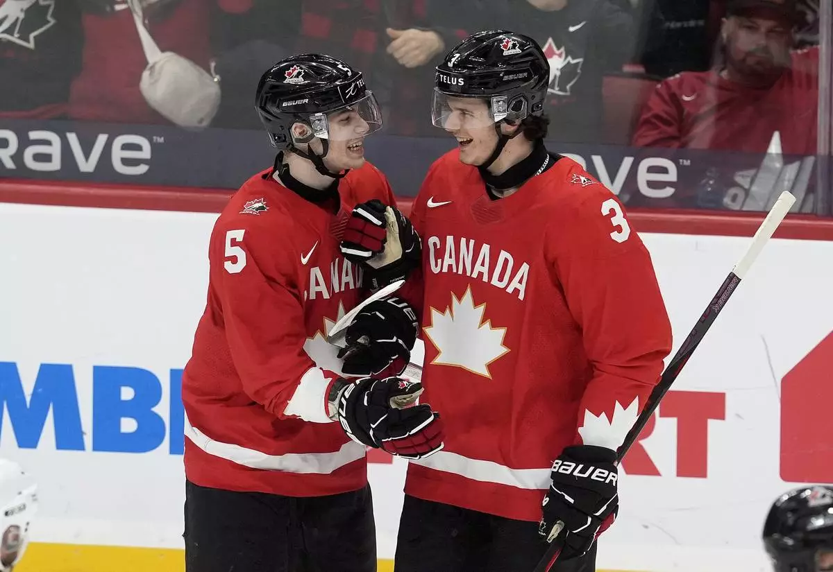 Canada defenseman Oliver Bonk (5) celebrates after his goal with teammate Sam Dickinson (3) during first-period IIHF World Junior Hockey Championship tournament game action against Germany in Ottawa, Ontario, Sunday, Dec. 29, 2024. (Adrian Wyld/The Canadian Press via AP)