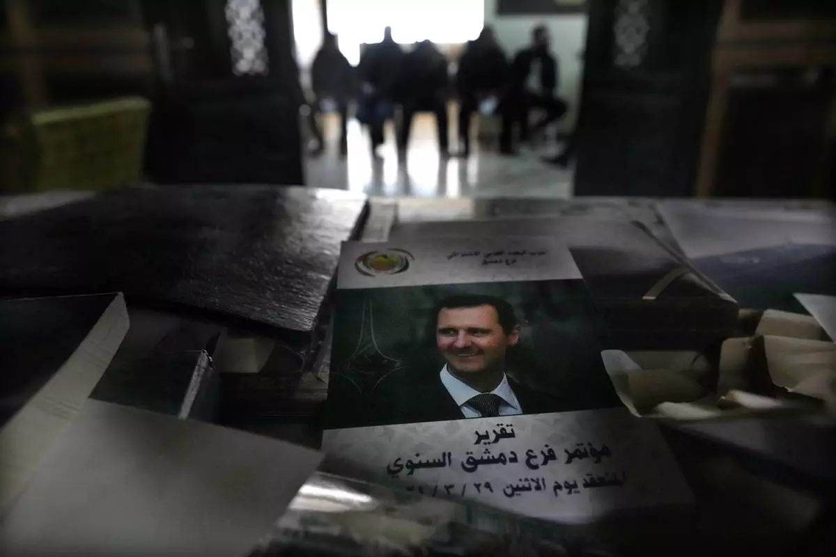 FILE.- A cover showing ousted Syrian President Bashar Assad, seen on a desk at the Baath party headquarter, as former army soldiers, background, wait to register their names with Syrian rebels as part of an "identification and reconciliation" process in Damascus, Syria, Monday, Dec. 23, 2024. (AP Photo/Hussein Malla,File)