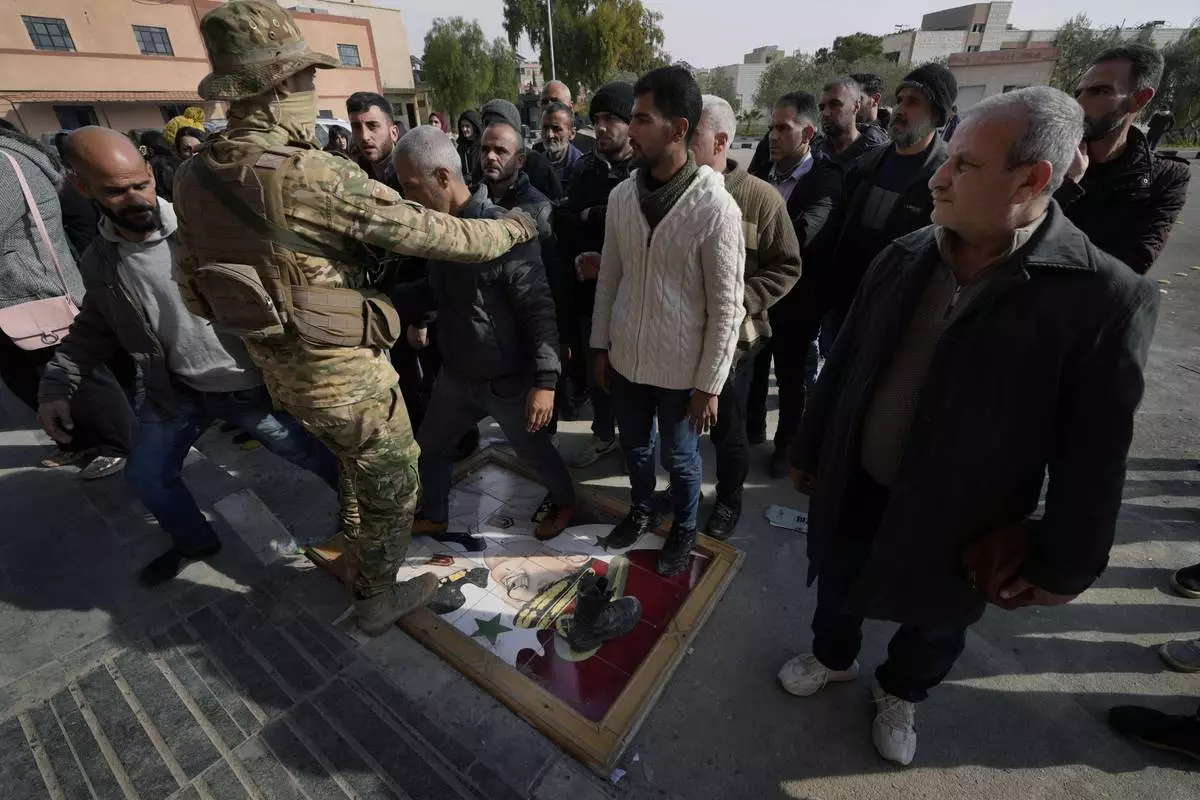 FILE.- A Syrian fighter, left, stands guard as members of ousted Syrian President Bashar Assad's army step on his portrait as a sign of disdain, lining up before they register their names with Syrian rebels as part of an "identification and reconciliation process" in Damascus, Syria, Monday, Dec. 23, 2024. (AP Photo/Hussein Malla,File)