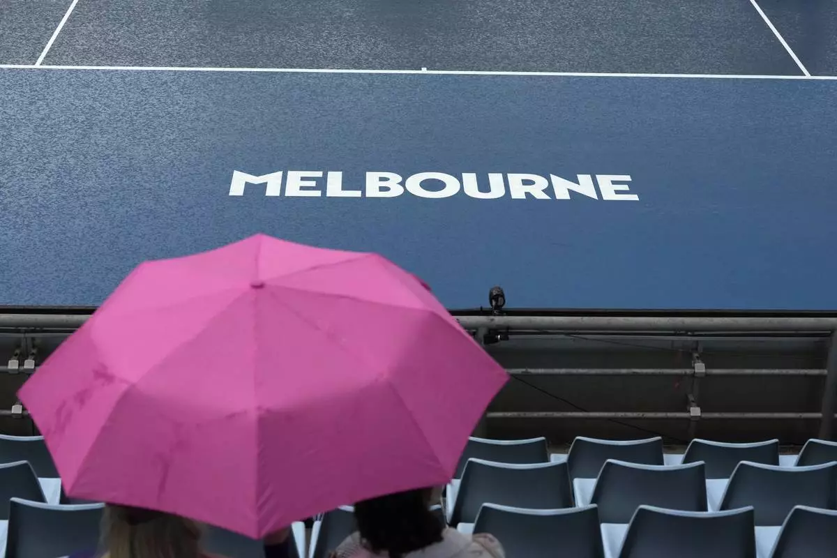 Zuschauer warten unter Sonnenschirmen, während der Regen das Spiel während der Erstrundenspiele der Australian Open-Tennismeisterschaft in Melbourne, Australien, Sonntag, 12. Januar 2025, unterbricht. (AP Photo/Manish Swarup)