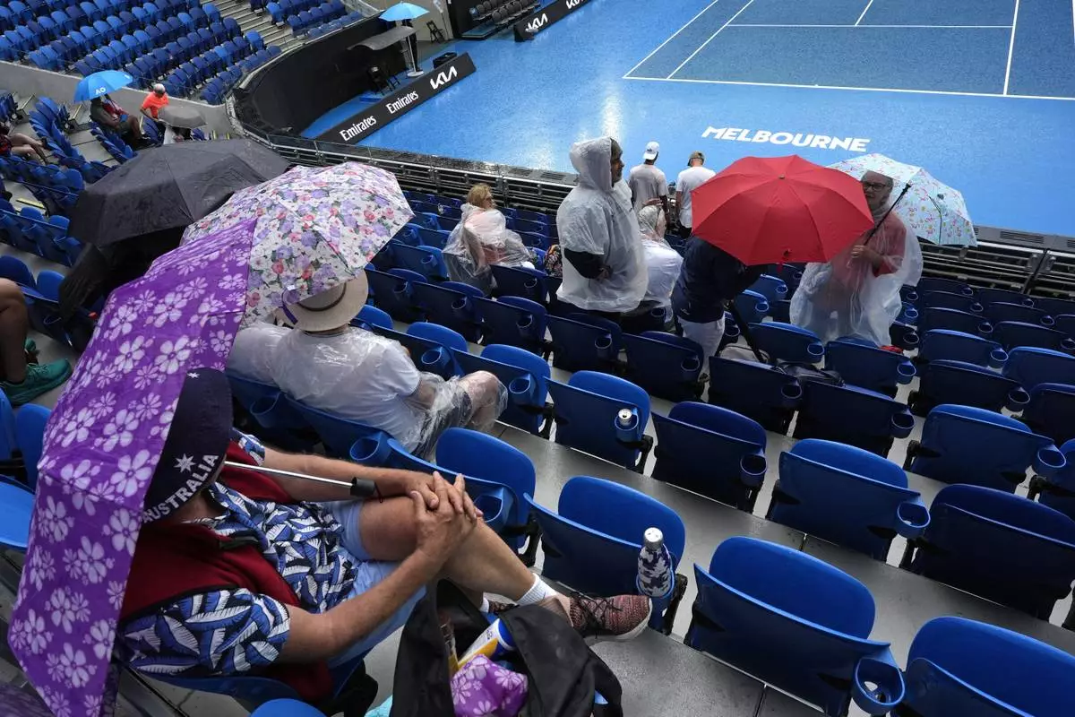 Zuschauer warten unter Sonnenschirmen, während der Regen das Spiel während der Erstrundenspiele der Australian Open-Tennismeisterschaft in Melbourne, Australien, Sonntag, 12. Januar 2025, unterbricht. (AP Photo/Asanka Brendon Ratnayake)