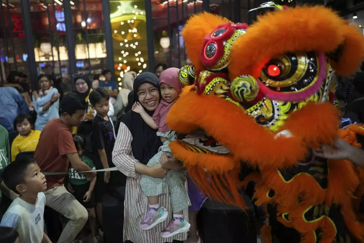 A Muslim woman and her daughter have their photo taken with members of dragon dance club Naga Merah Putih (Red White Dragon) in lion costume after a performance at a shopping mall in Bogor, West Java, Indonesia, Sunday, Jan. 26, 2025. (AP Photo/Dita Alangkara)
