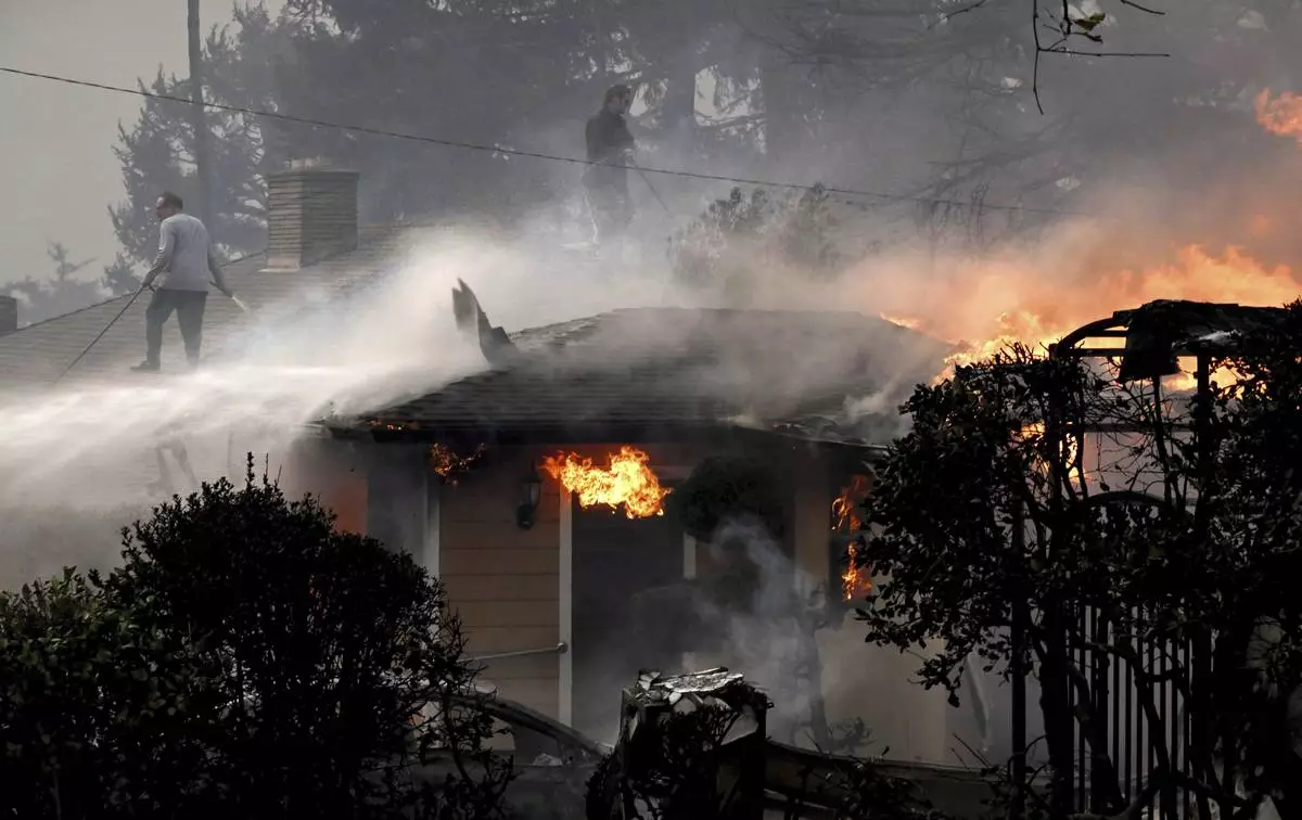 Eric Fiedler, left, and his son Christopher spray water on their roof in an attempt to save it along Sinaloa Avenue as his next door neighbors home burns during the Eaton fire in Altadena Wednesday morning Jan. 8, 2025. (Will Lester/The Orange County Register via AP)