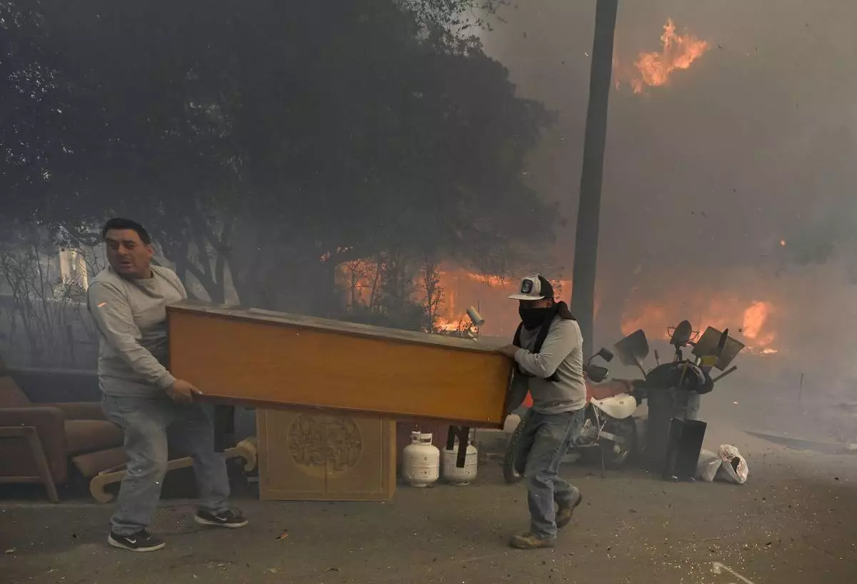 Residents along Braeburn Road rush to save property as a home burns behind them during the Eaton fire in Altadena Wednesday morning Jan. 8, 2025. (Will Lester/The Orange County Register via AP)