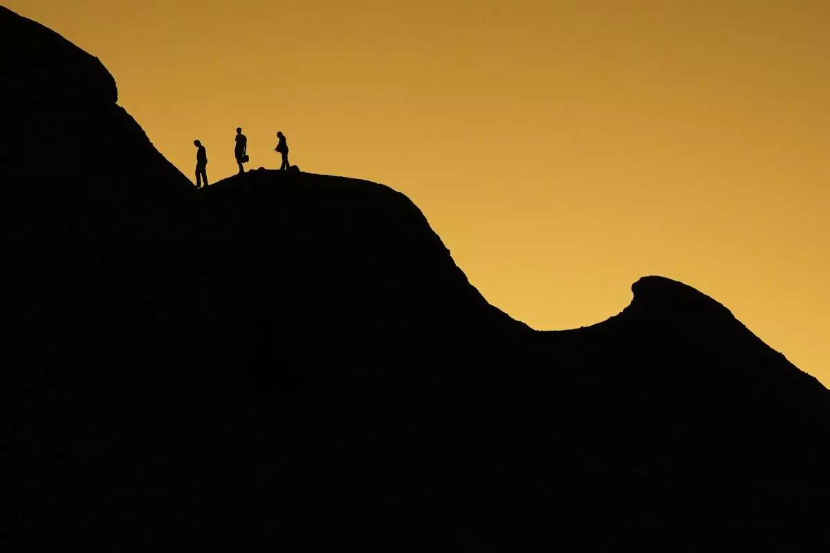 People walk on top of the Hole in the Rock formation as the sun sets at Papago Park, Tuesday, Feb. 25, 2025, in Phoenix. (AP Photo/Lindsey Wasson)