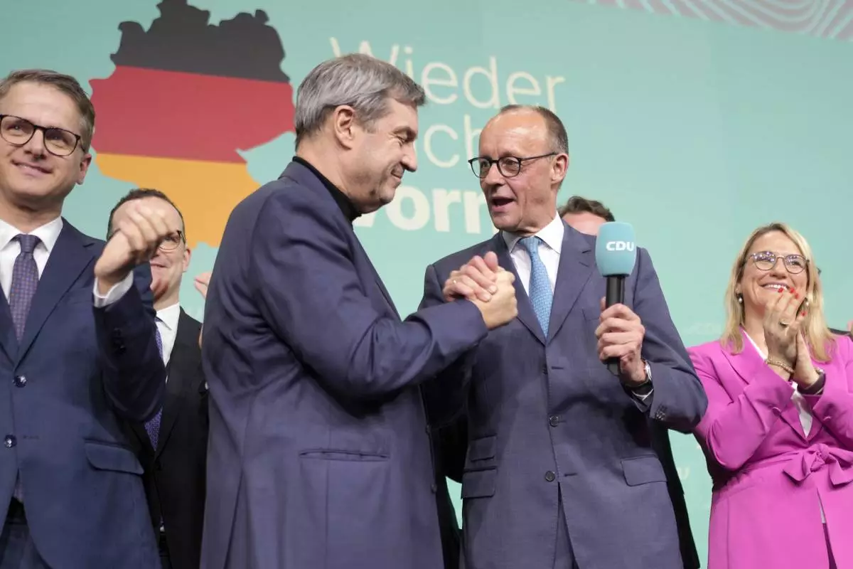 Friedrich Merz, with the microphone, the candidate of the mainstream conservative Christian Democratic Union party, shakes hands with Markus Soeder, leader of CSU and Minister-President of Bavaria, at the party headquarters in Berlin, Germany, Sunday, Feb. 23, 2025, after the German national election. (AP Photo/Markus Schreiber)