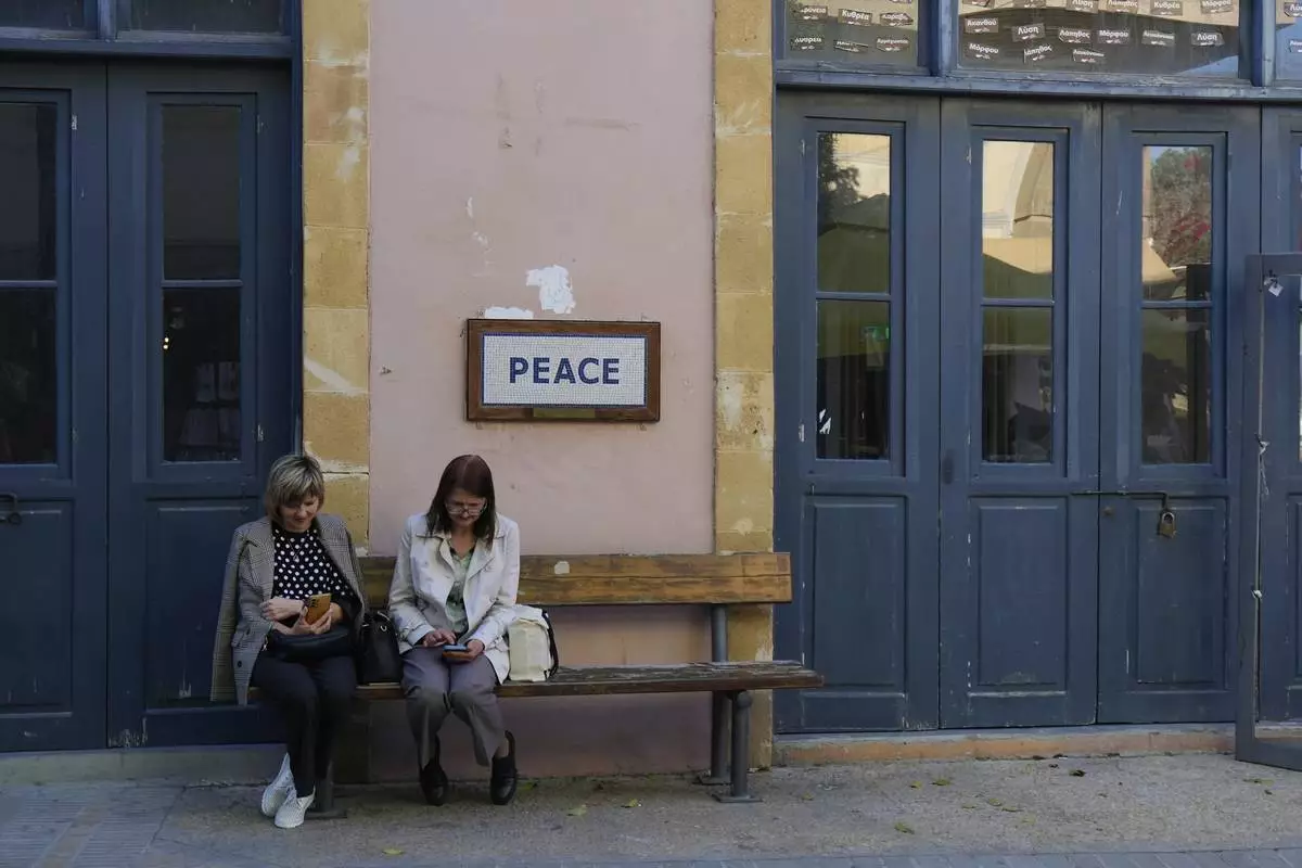 Women sit on a bench next to a checkpoint crossing point at Ledra street in divided capital Nicosia, Cyprus, Tuesday, March 18, 2025. (AP Photo/Petros Karadjias)