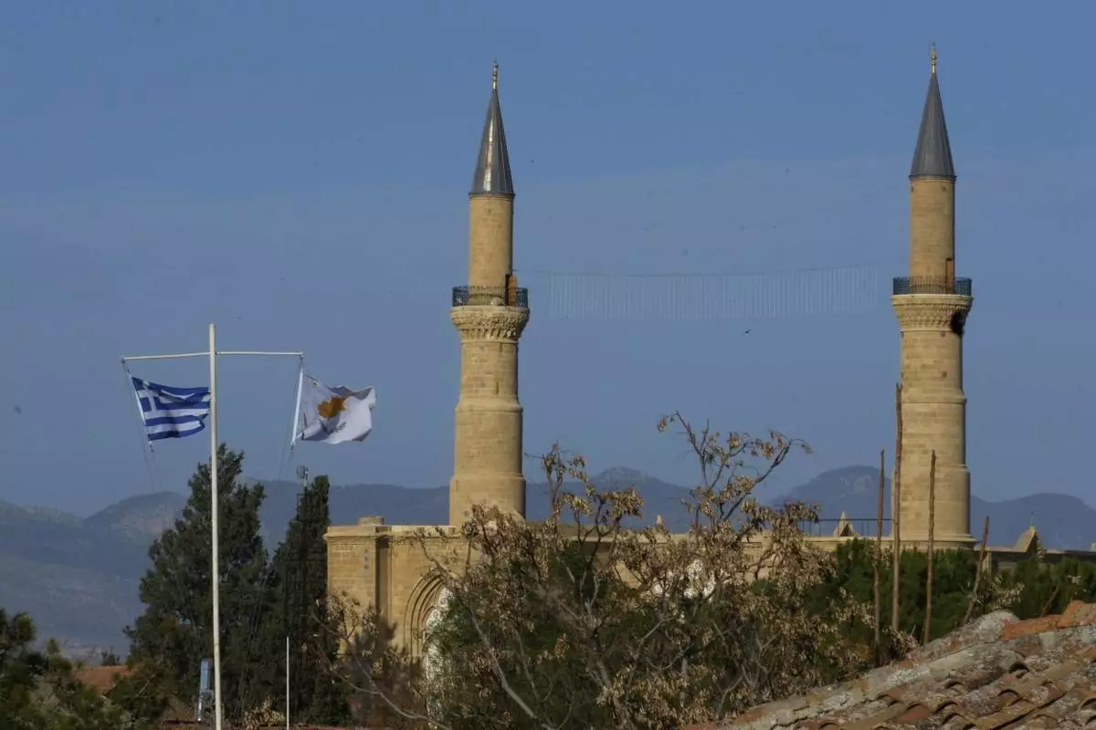 A Cyprus' and a Greek flags, are seen on the pols in the south, as in the background are seen the minarets of the Selimiye mosque, or Cathedral of St Sophia, or Agia Sofia, in the Turkish occupied area in the north, in divided capital Nicosia, Cyprus, Tuesday, March 18, 2025. (AP Photo/Petros Karadjias)