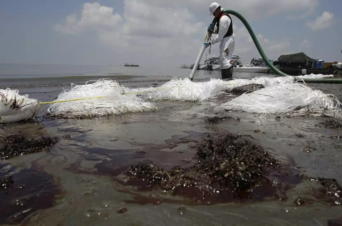FILE - A worker uses a suction hose to remove oil washed ashore from the Deepwater Horizon spill, in Belle Terre, La., June 9, 2010. (AP Photo/Eric Gay, File)