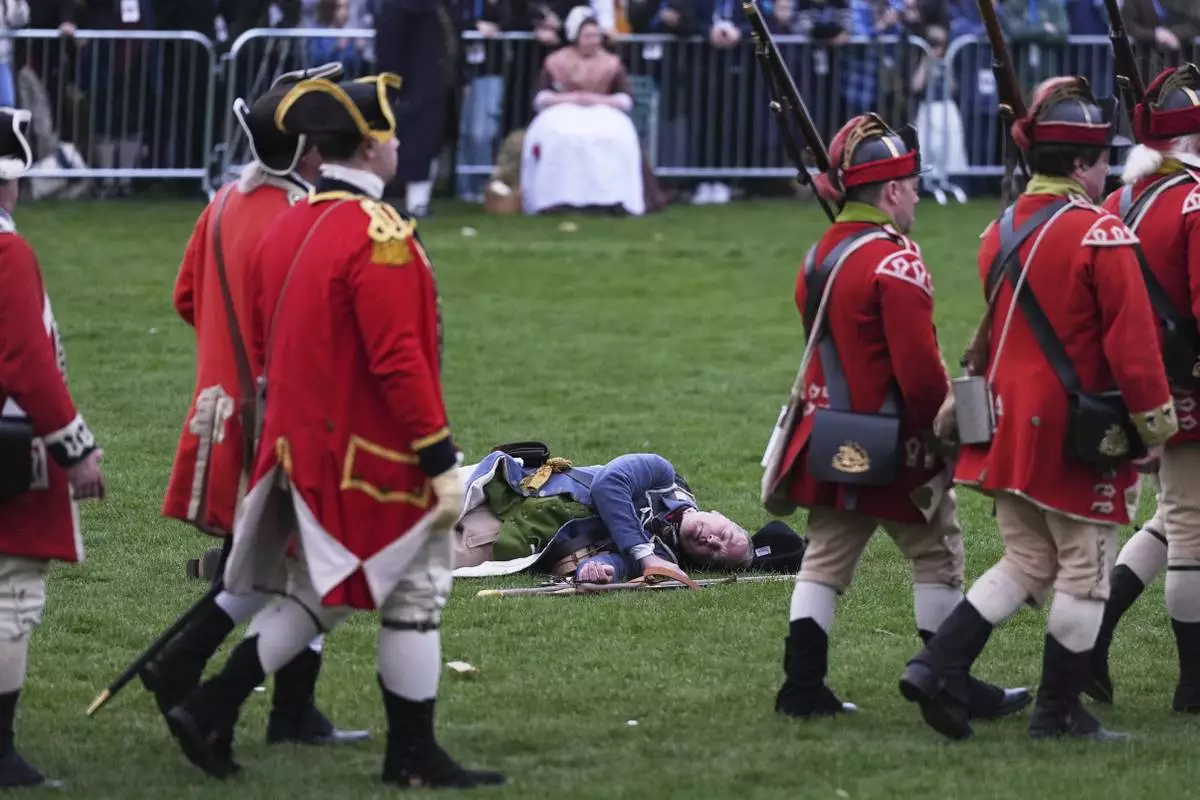 British Regulars march past a fallen New England colonial militia, also known as a Minuteman, during a reenactment celebration of the 250th anniversary of the Battle of Lexington and start of the American Revolution, Saturday, April 19, 2025, in Lexington, Mass. (AP Photo/Charles Krupa)