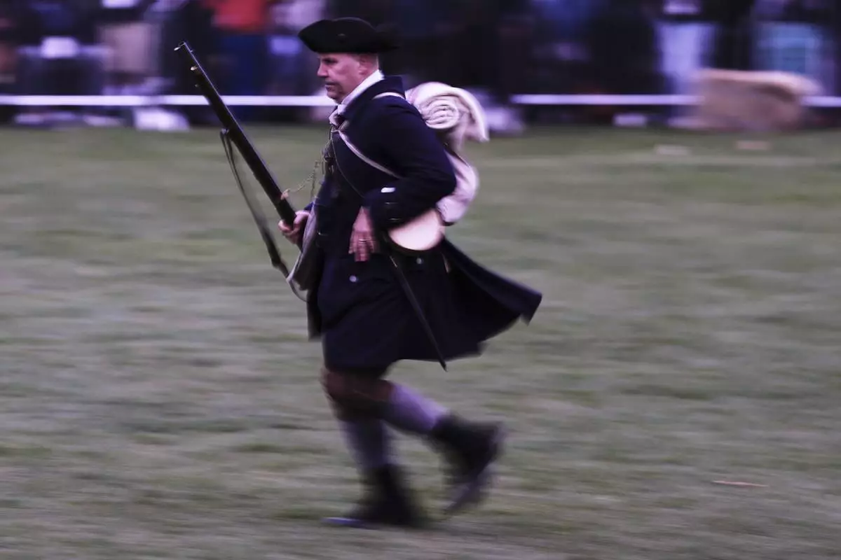 New England colonial militia man, also known as a Minuteman, runs towards fellow troops before sunrise during a reenactment celebration of the 250th anniversary of the Battle of Lexington and start of the American Revolution, Saturday, April 19, 2025, in Lexington, Mass. (AP Photo/Charles Krupa)