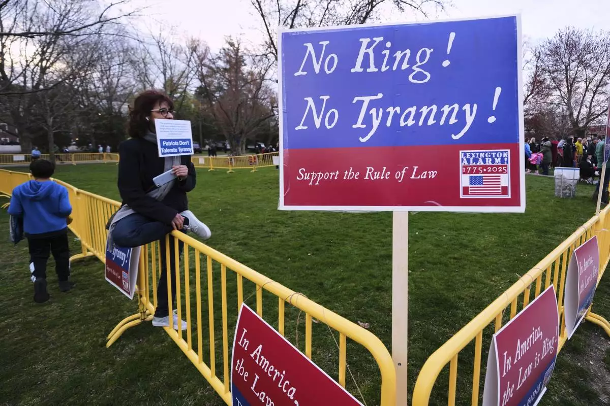 A lone protestor sits in the "Free Speech Zone" during a reenactment celebration of the 250th anniversary of the Battle of Lexington and start of the American Revolution, Saturday, April 19, 2025, in Lexington, Mass. (AP Photo/Charles Krupa)