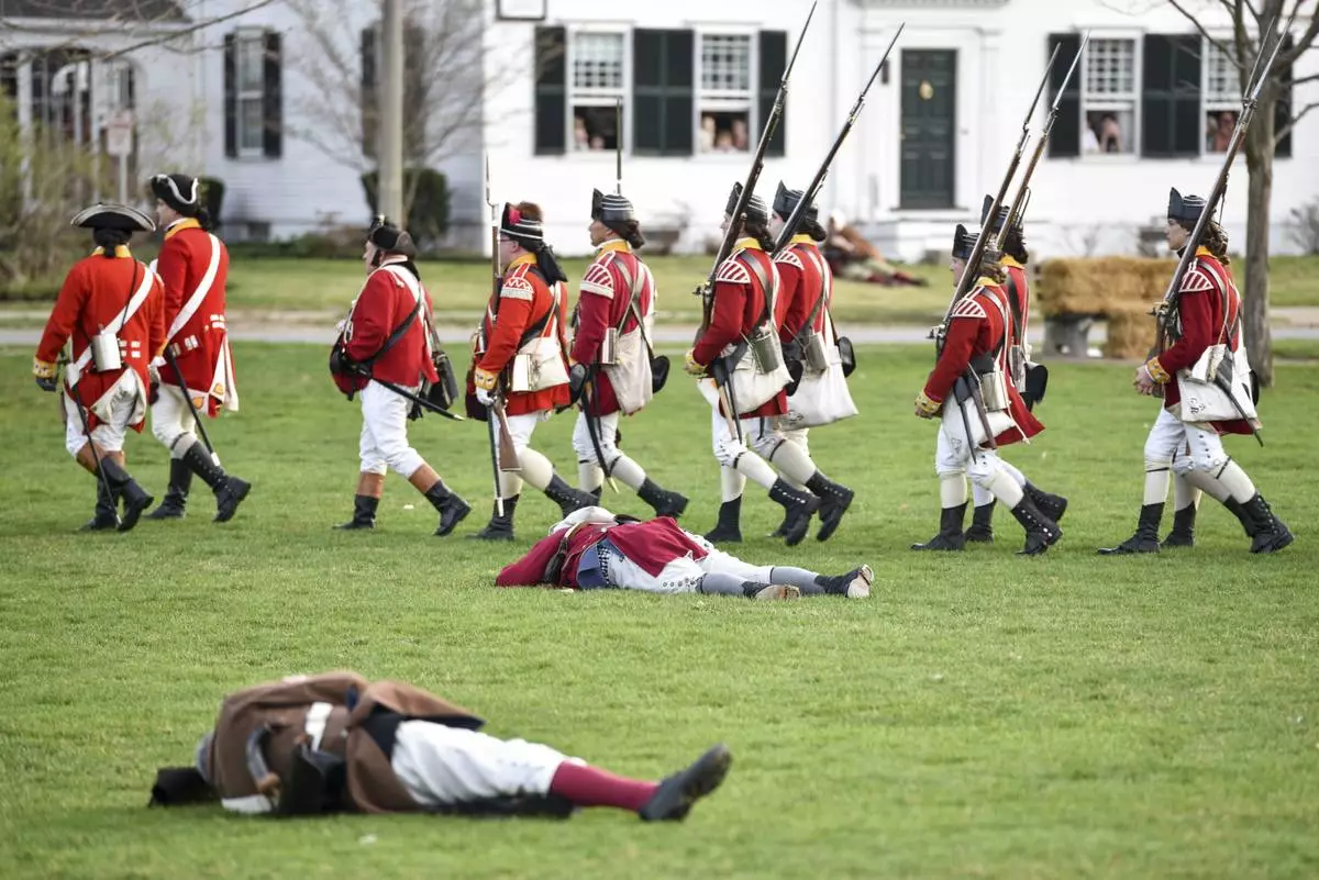 FILE - British re-enactors march past dead Colonial soldiers during the Patriots' Day re-enactment during the Patriots' Day reenactment of the battles of Lexington and Concord, on the Lexington Green in Lexington, Mass. Monday, Aril 17, 2017. (Keith Viglione/The Boston Herald via AP,FIle)