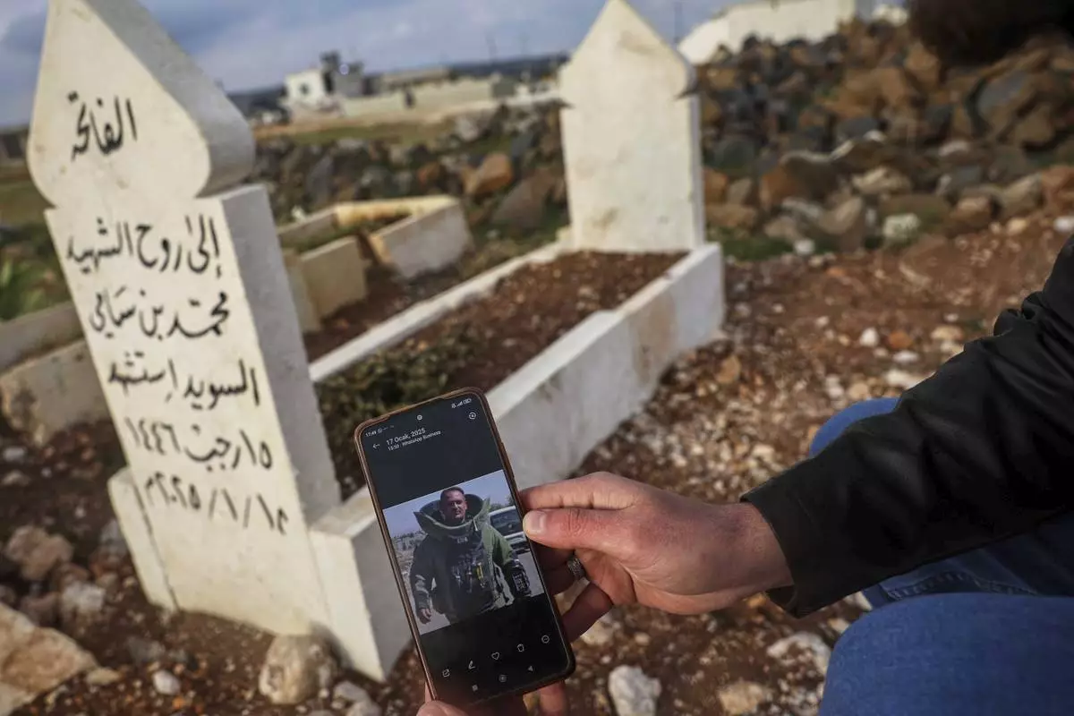 Salah Swed , 28, holds a cellphone showing a picture of his brother Mohammed, killed while attempting to dismantle a landmine, as he visits his grave in their village of Kafr Nabl, south of Idlib, Syria, Monday, April 14, 2025.(AP Photo/Ghaith Alsayed)