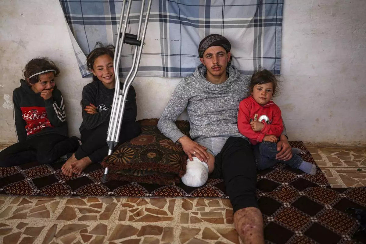 Suleiman Khalil, 21, who lost his leg in a landmine explosion while harvesting olives with his friends in a field, poses for a pictures with his siblings from left to right, Sakina, 8, Nahla, 9, and Aya, 5, at his home in the village of Qaminas, east of Idlib, Syria, Wednesday, April 9, 2025. (AP Photo/Ghaith Alsayed)