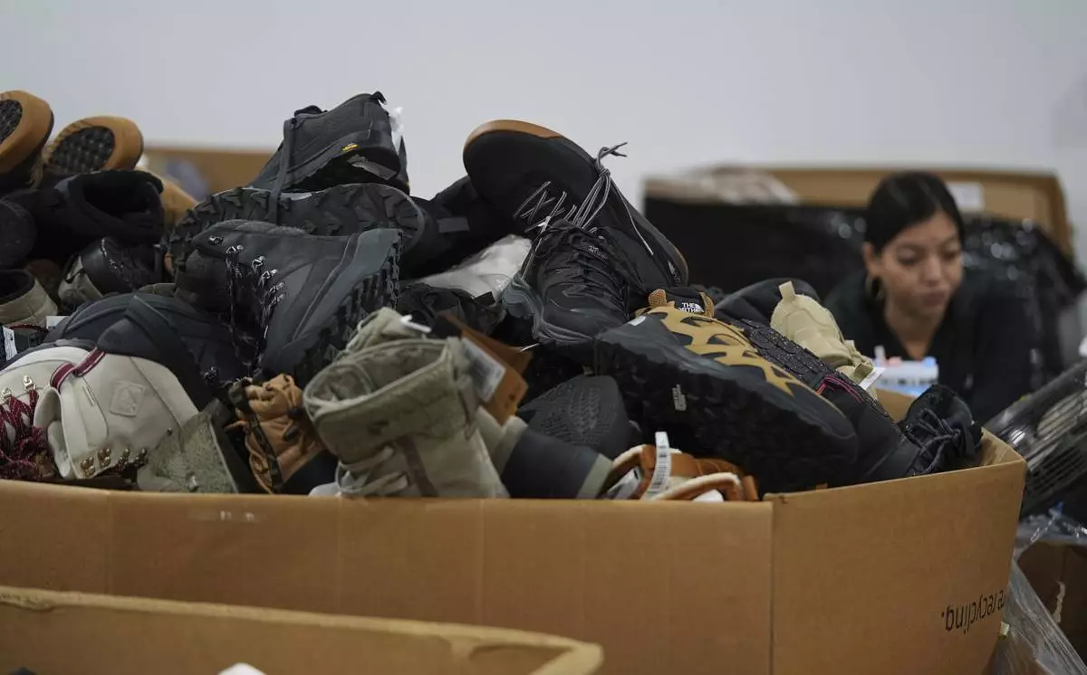 People work amid boxes of returned or overstocked clothing, shoes, boots, coats, packs and other items in a warehouse where the goods are cleaned or repaired before they are marketed on resale platforms in Englewood, Colo., on Thursday, April 17, 2025. (AP Photo/David Zalubowski)