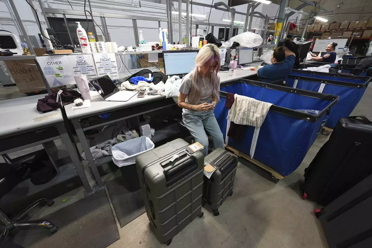 A woman works amid boxes of returned or overstocked clothing, shoes, boots, coats, packs and other items in a warehouse where the goods are cleaned or repaired before they are marketed on resale platforms in Englewood, Colo., on Thursday, April 17, 2025. (AP Photo/David Zalubowski)