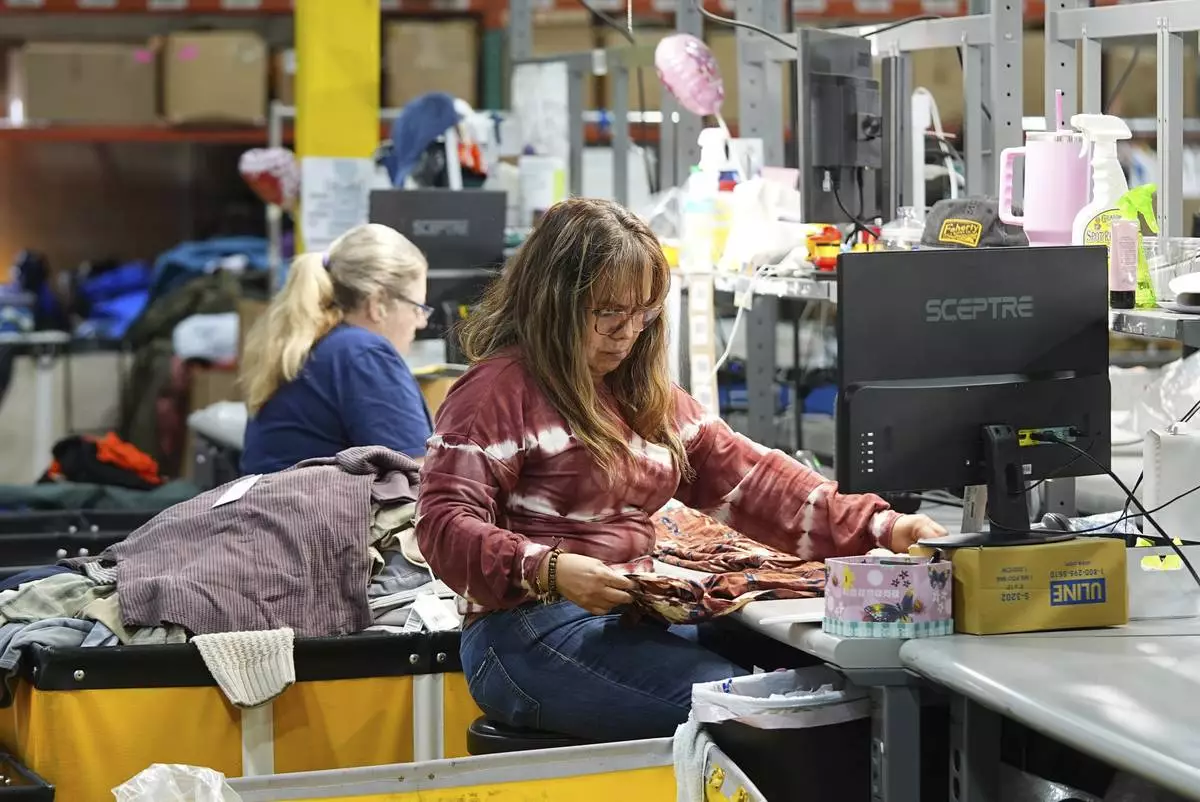 People work amid boxes of returned or overstocked clothing, shoes, boots, coats, packs and other items in a warehouse where the goods are cleaned or repaired before they are marketed on resale platforms in Englewood, Colo., on Thursday, April 17, 2025. (AP Photo/David Zalubowski)