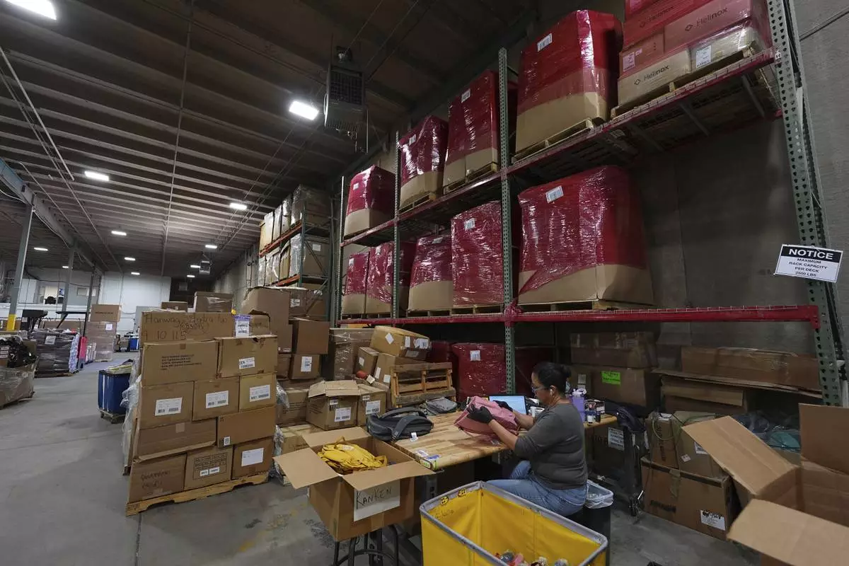 People work amid boxes of returned or overstocked clothing, shoes, boots, coats, packs and other items in a warehouse where the goods are cleaned or repaired before they are marketed on resale platforms in Englewood, Colo., on Thursday, April 17, 2025. (AP Photo/David Zalubowski)