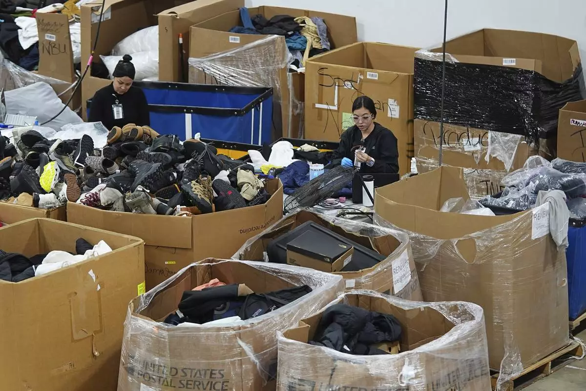People work amid boxes of returned or overstocked clothing, shoes, boots, coats, packs and other items in a warehouse where the goods are cleaned or repaired before they are marketed on resale platforms in Englewood, Colo., on Thursday, April 17, 2025. (AP Photo/David Zalubowski)