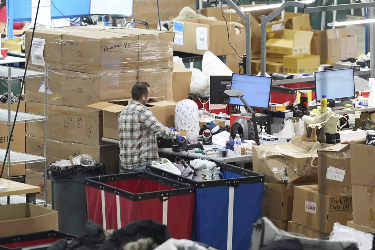 A man works amid boxes of returned or overstocked clothing, shoes, boots, coats, packs and other items in a warehouse where the goods are cleaned or repaired before they are marketed on resale platforms in Englewood, Colo., on Thursday, April 17, 2025. (AP Photo/David Zalubowski)