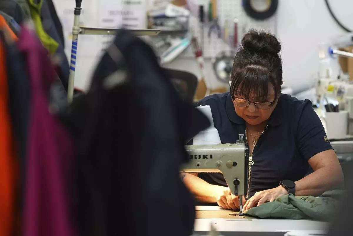 A worker sews a coat in a warehouse where the goods from various clothing manufacturers are cleaned or repaired before they are marketed on resale platforms Thursday, April 17, 2025, in Englewood, Colo. (AP Photo/David Zalubowski)