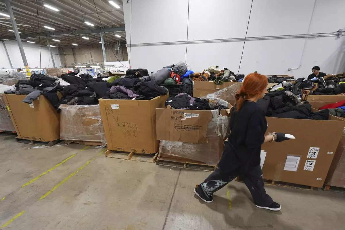 A worker walks past boxes of returned or overstocked clothing, shoes, boots, coats, packs and other items in a warehouse where the goods are cleaned or repaired before they are marketed on resale platforms in Englewood, Colo., on Thursday, April 17, 2025. (AP Photo/David Zalubowski)