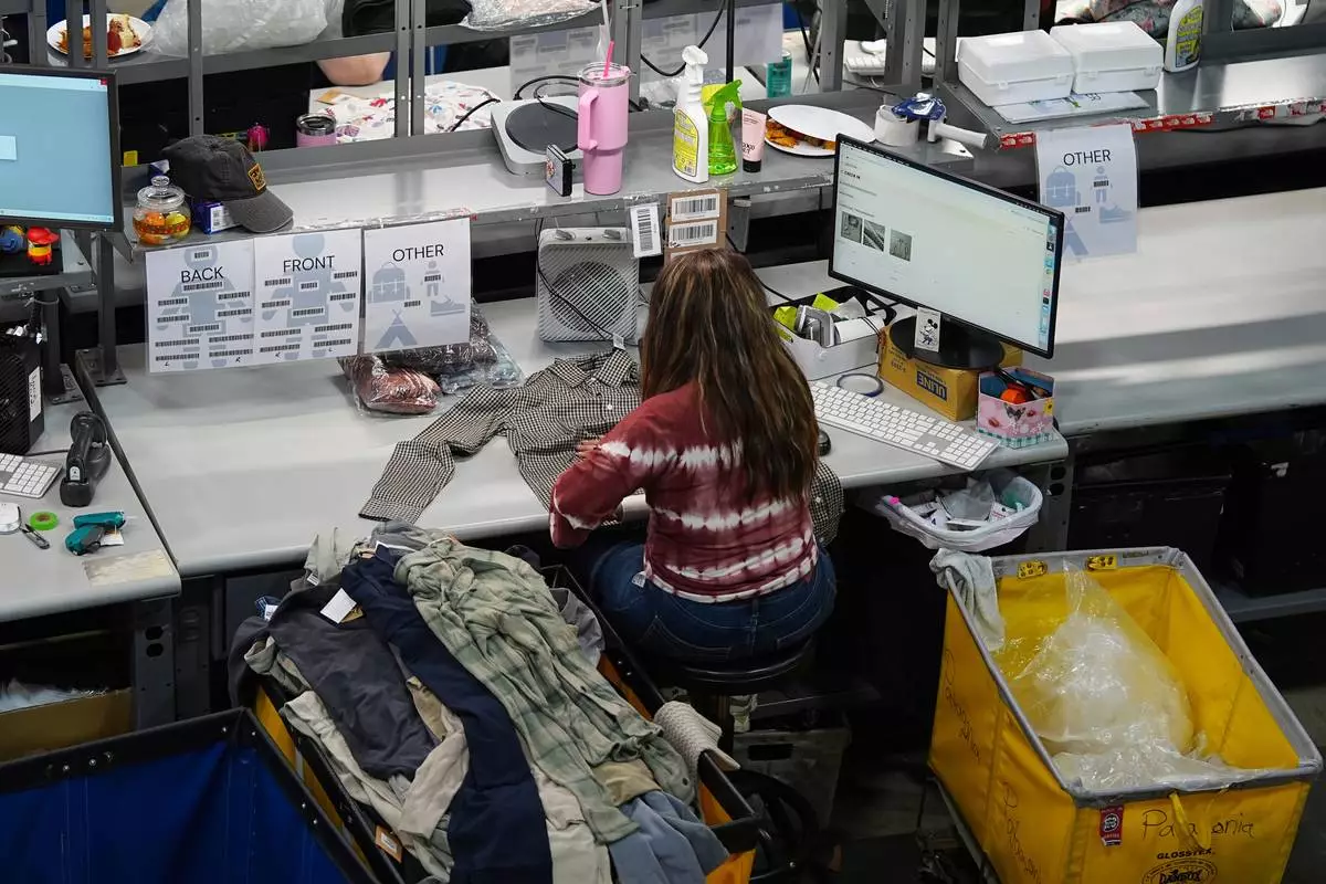 People work amid boxes of returned or overstocked clothing, shoes, boots, coats, packs and other items in a warehouse where the goods are cleaned or repaired before they are marketed on resale platforms in Englewood, Colo., on Thursday, April 17, 2025. (AP Photo/David Zalubowski)