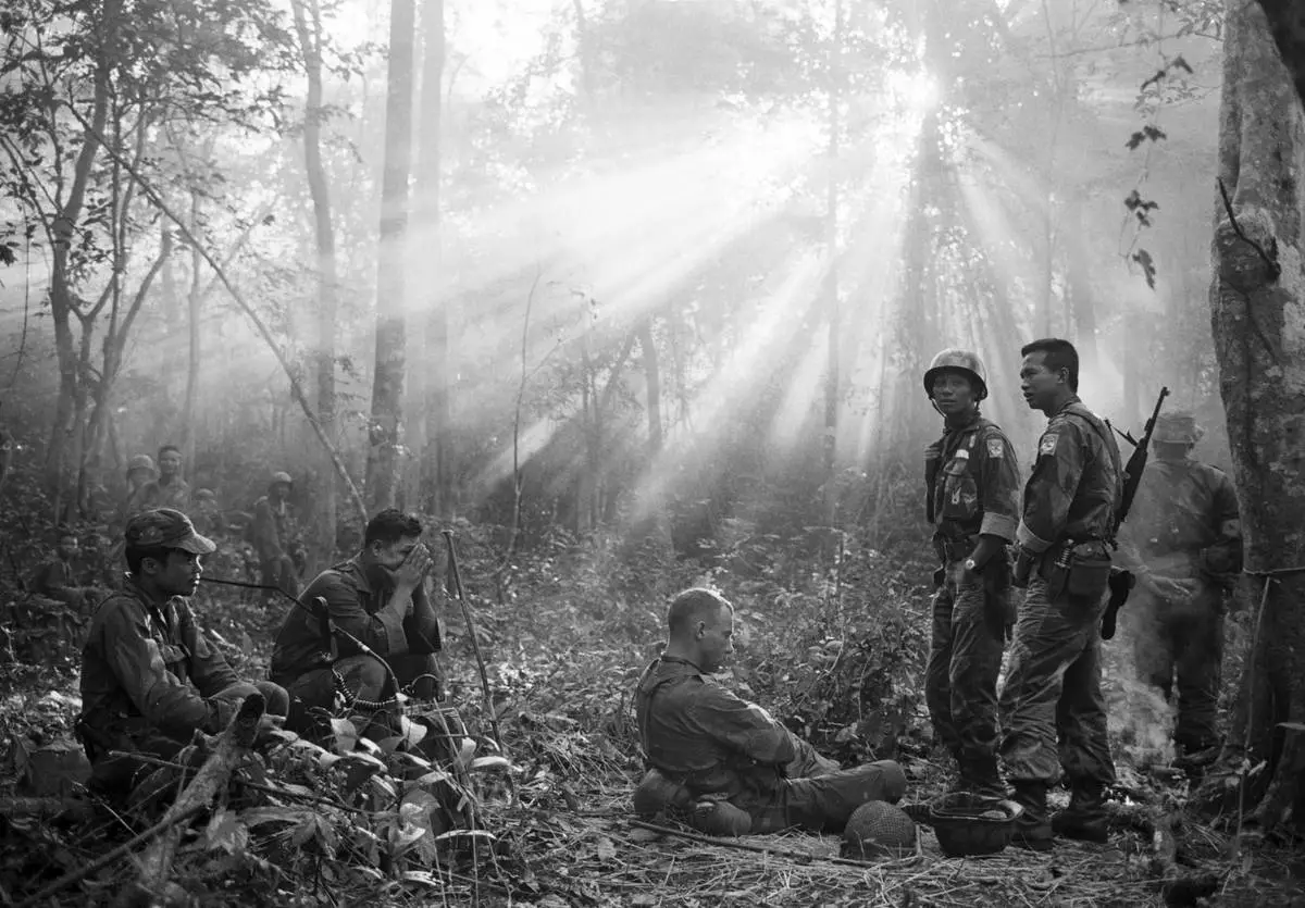 FILE- The sun breaks through the dense jungle foliage around the embattled town of Binh Gia, 40 miles east of Saigon, in early January 1965, as South Vietnamese troops, apparently joined by U.S. advisers, rest after a cold, damp and tense night of waiting in an ambush position for a Viet Cong attack that didn't come. One hour later, as the possiblity of an overnight attack by the Viet Cong diasappeared, the troops moved out for another long, hot day hunting the elusive communist guerrillas in the jungles. (AP Photo/Horst Faas, File)