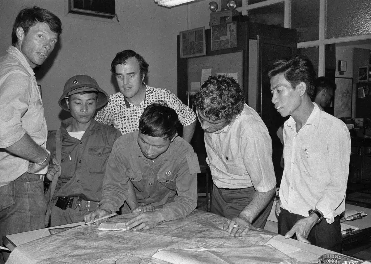 The last three staffers in The Associated Press' Saigon bureau, reporters Matt Franjola, left, Peter Arnett, rear, and George Esper, second from right, are joined by two North Vietnamese soldiers and a member of the Viet Cong on the day the government of South Vietnam surrendered, April 30, 1975. One of the soldiers is showing Esper the route of his final advance into the city. (AP Photo/Sarah Errington)