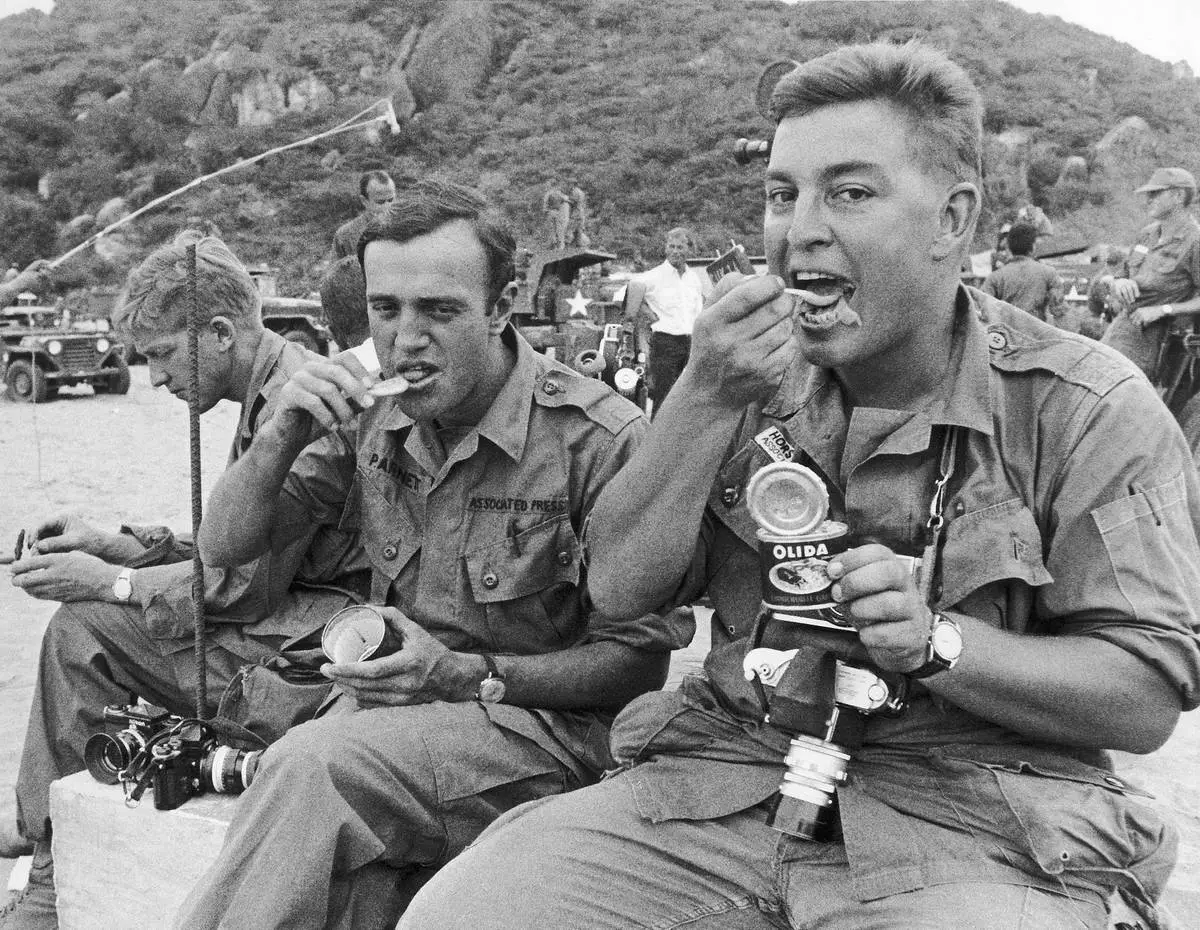 AP correspondent Peter Arnett and AP staff photographer Horst Faas eat while waiting for the arrival of the U.S. 1st Division in July 1965 in Cam Ranh Bay. Faas eats a French-made sausage sauerkraut meal from a can while Arnett has a C-ration. (AP Photo/AP Corporate Archives)