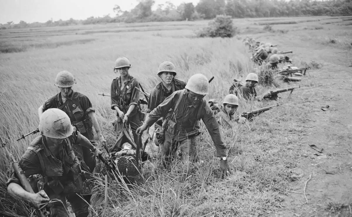 FILE- U.S. corpsmen carry the body of a dead Marine as fellow Marines crouch along a road through a rice paddy, about a mile south of the demilitarized zone, in September 1966. The Marines had taken heavy automatic weapons fire from the treeline at the edge of the paddy. (AP Photo/Horst Faas)