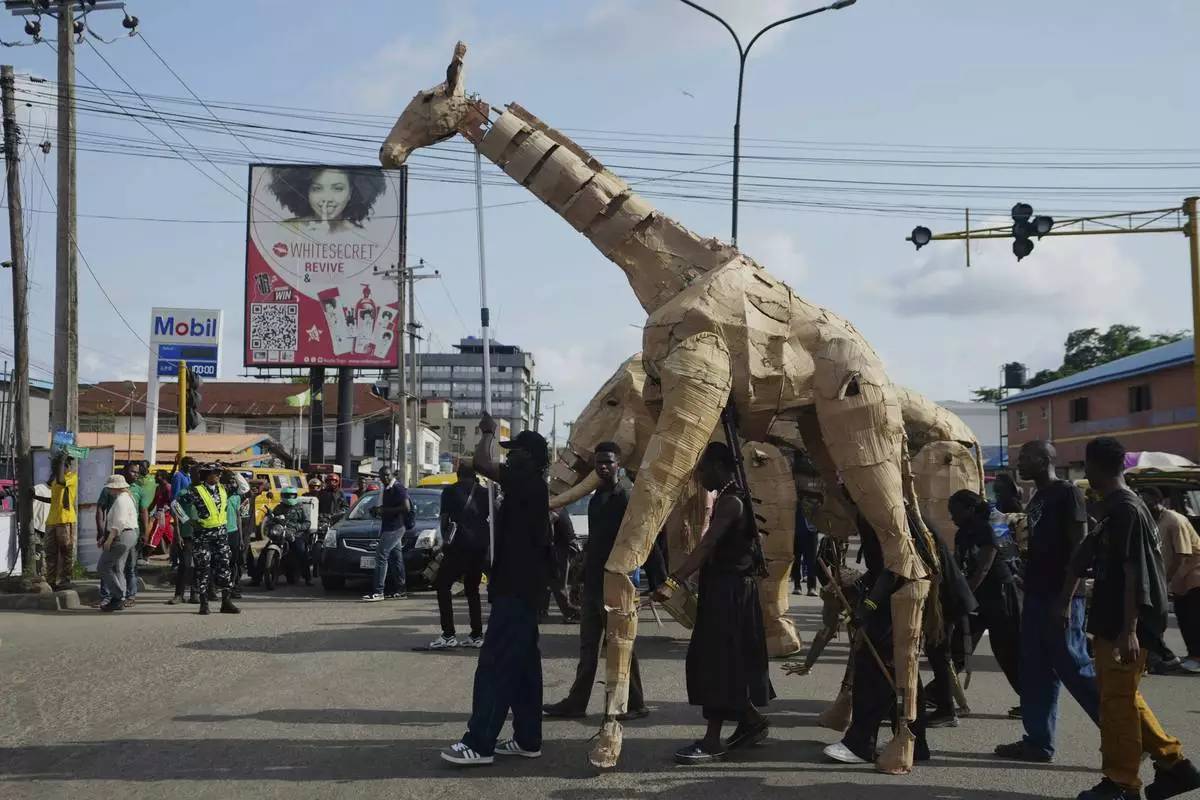 Puppeteers move cardboard animals on the street of Lagos Nigeria, Saturday, April 19, 2025, as part of "The Herds," a moving theatre performance that started its journey from the Democratic Republic of the Congo to the Arctic Circle in a bid to bring attention to the climate crisis. (AP Photo/Sunday Alamba)