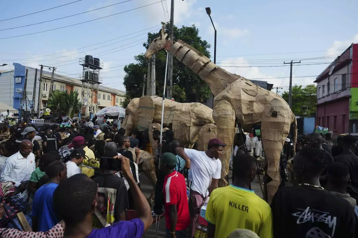 Puppeteers move cardboard animals on the street of Lagos Nigeria, Saturday, April 19, 2025, as part of "The Herds," a moving theatre performance that started its journey from the Democratic Republic of the Congo to the Arctic Circle in a bid to bring attention to the climate crisis. (AP Photo/Sunday Alamba)