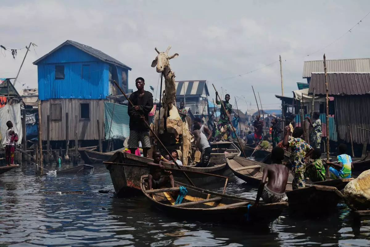 Puppeteers move cardboard animals in canoes at the Makoko Slum in Lagos Nigeria, Saturday, April 19, 2025, as part of "The Herds," a moving theatre performance that started its journey from the Democratic Republic of the Congo to the Arctic Circle in a bid to bring attention to the climate crisis. (AP Photo/Sunday Alamba)