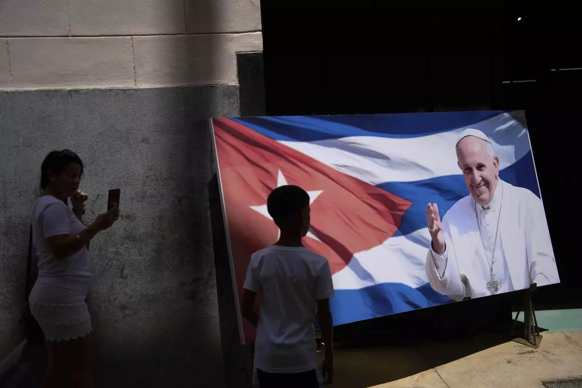 People take photos by a photo of Pope Francis at the entrance to the car museum where one of the Popemobiles he used during his visit to Cuba is displayed in Havana, Tuesday, April 22, 2025. (AP Photo/Ramon Espinosa)