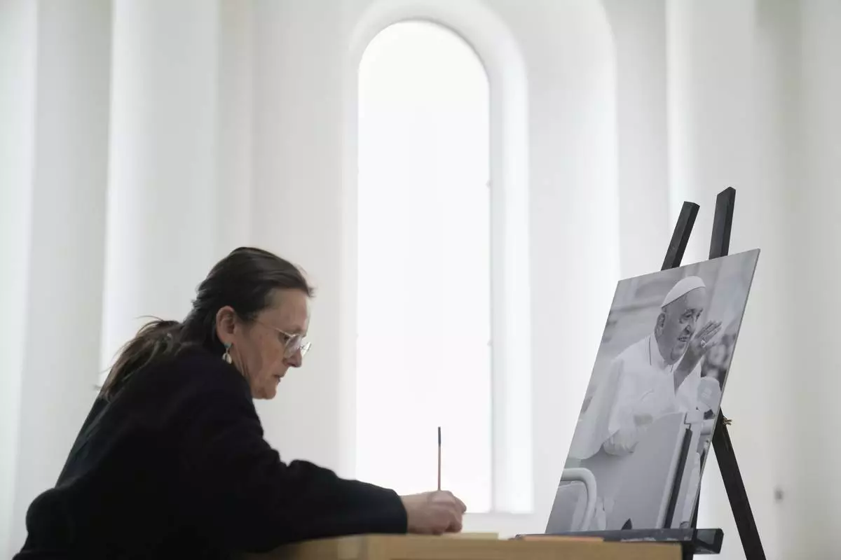 A woman writes in a condolence book for the late Pope Francis at the Saint Hedwig's Cathedral in Berlin, Germany, Tuesday, April 22, 2025. (AP Photo/Ebrahim Noroozi)